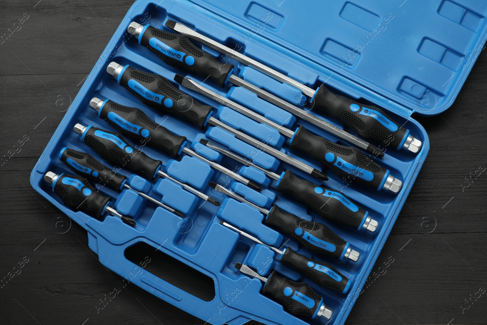 Photo of Set of screwdrivers in open toolbox on black wooden table, top view