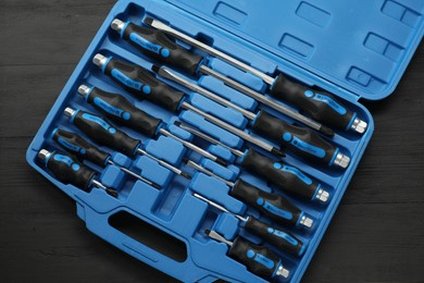 Set of screwdrivers in open toolbox on black wooden table, top view