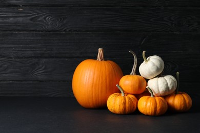 Photo of Thanksgiving day. Beautiful composition with pumpkins on table against black wooden wall, space for text