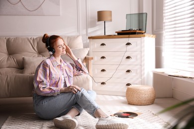 Photo of Young woman listening to music with turntable in living room