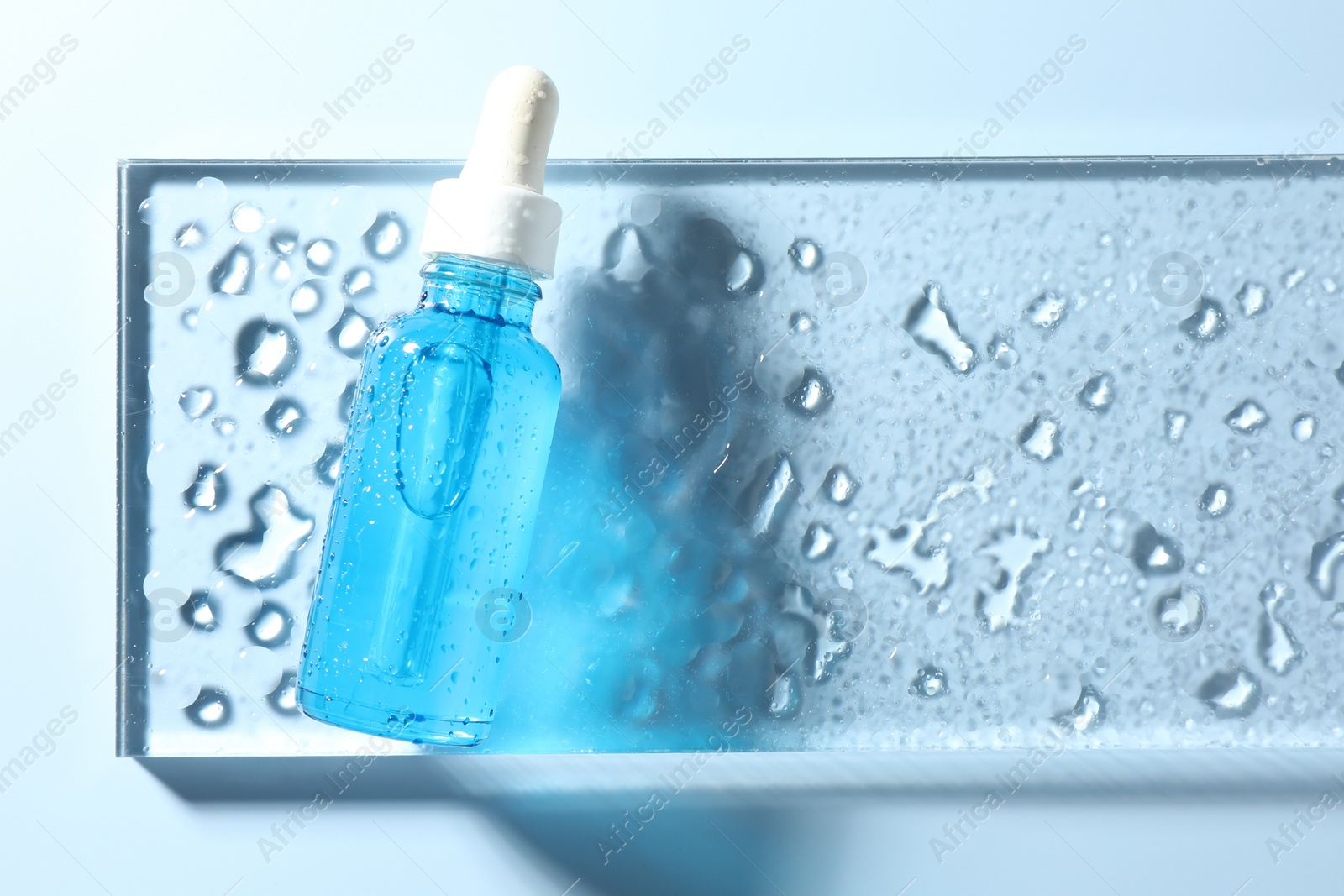 Photo of Bottle of cosmetic serum on light blue background, top view