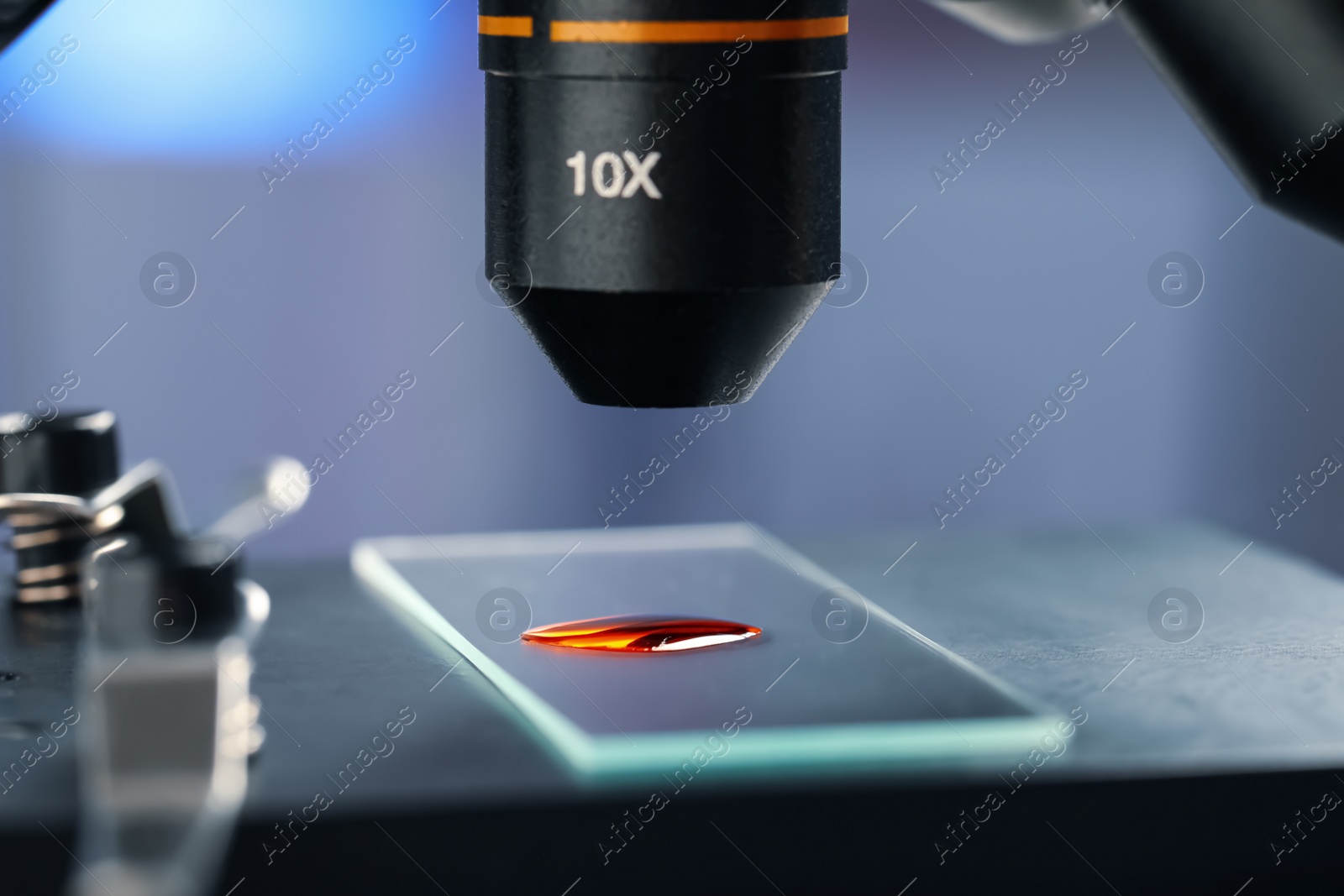 Photo of Glass slide with sample of red liquid under microscope in laboratory, closeup