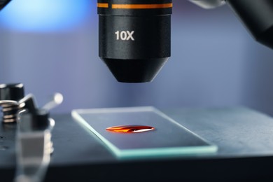 Photo of Glass slide with sample of red liquid under microscope in laboratory, closeup