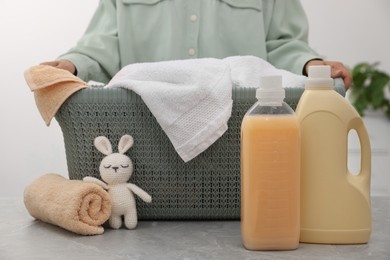 Woman holding basket with towels and bottles of laundry detergents indoors, closeup