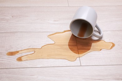 Photo of White mug with spilled liquid on wooden floor