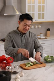 Cooking process. Man cutting fresh cucumber at countertop in kitchen