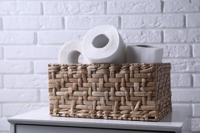 Photo of Toilet paper rolls in wicker basket on chest of drawers near white brick wall