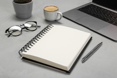 Photo of Open notebook, pen, laptop and glasses on light grey table