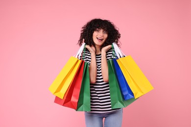 Happy young woman with shopping bags on pink background