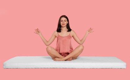 Photo of Young woman meditating on soft mattress against pale pink background