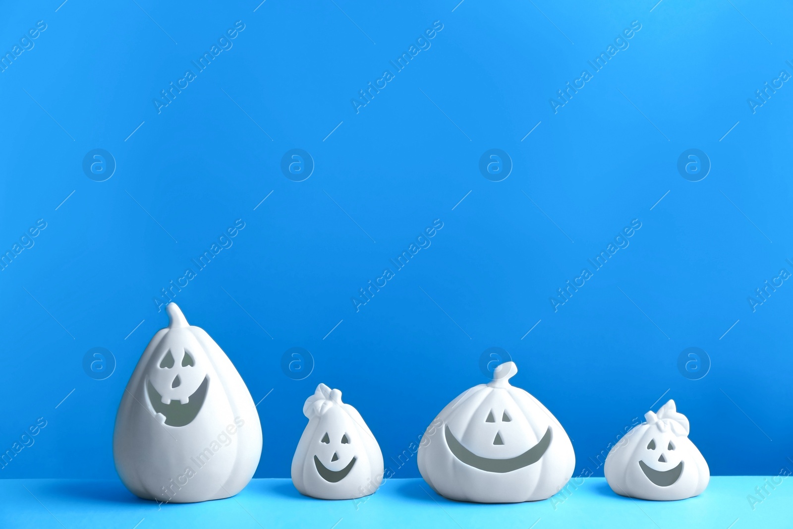 Photo of White pumpkin shaped candle holders on blue background, space for text. Halloween decoration