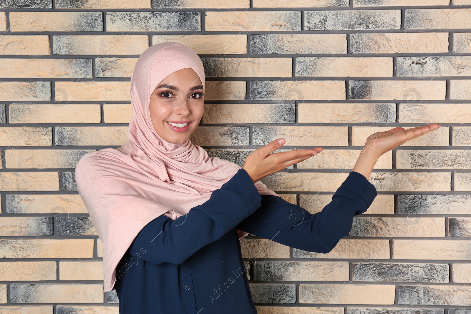 Photo of Portrait of young Muslim woman in hijab against brick wall