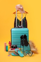 Photo of Suitcase, clothes and beach accessories on yellow background. Summer vacation