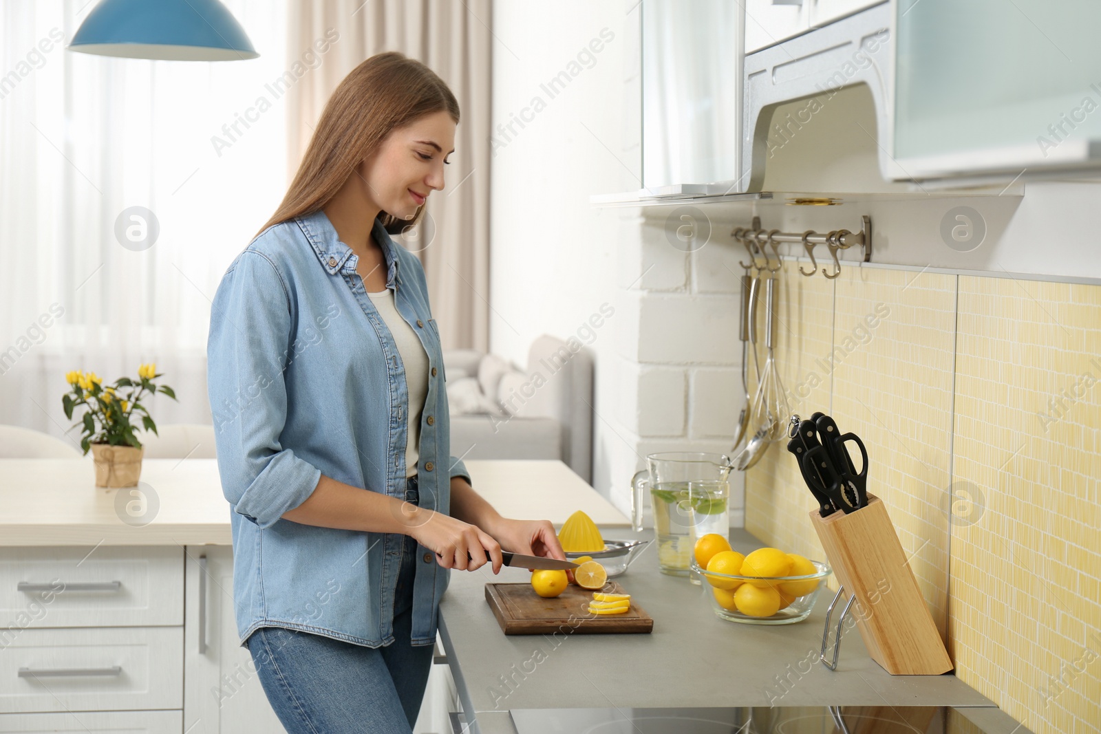 Photo of Young woman cutting lemon for refreshing drink in kitchen