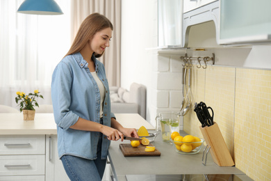 Photo of Young woman cutting lemon for refreshing drink in kitchen