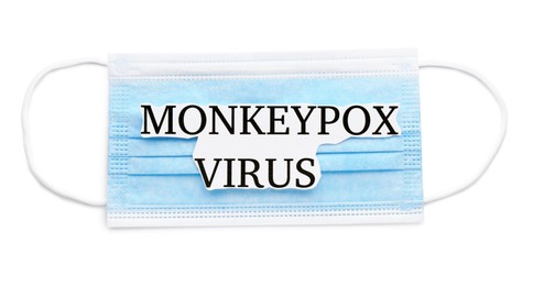 Photo of Medical face mask with words Monkeypox Virus on white background, top view