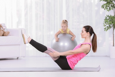 Photo of Sportive woman doing fitness exercises with daughter at home