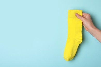 Photo of Woman holding yellow sock on light blue background, closeup. Space for text