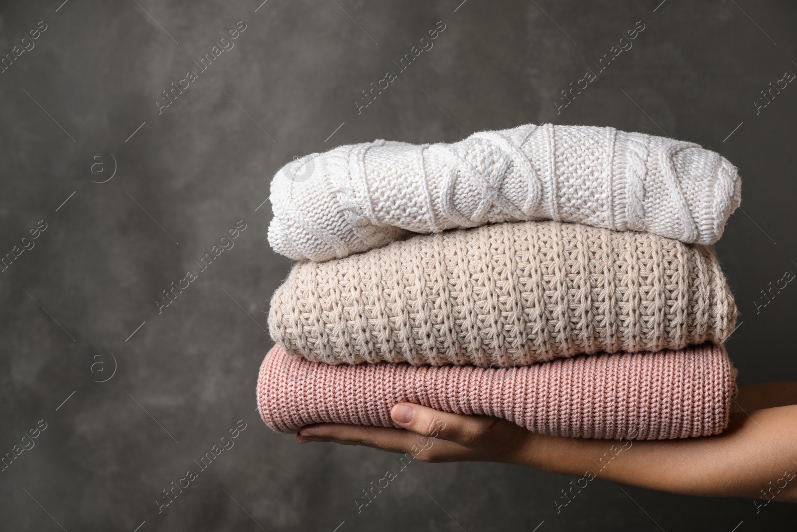 Photo of Woman holding stack of folded warm knitted sweaters against dark background