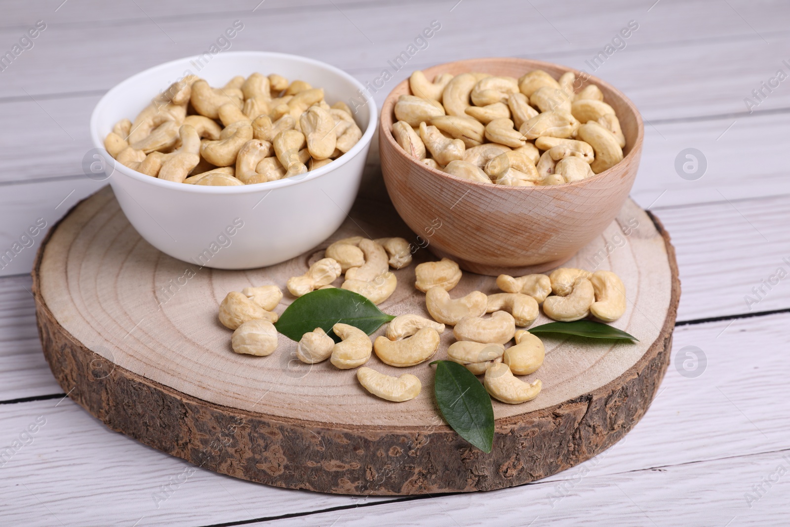 Photo of Tasty cashew nuts and green leaves on light wooden table