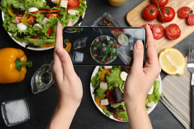 Blogger taking photo of fresh salad at black table, closeup