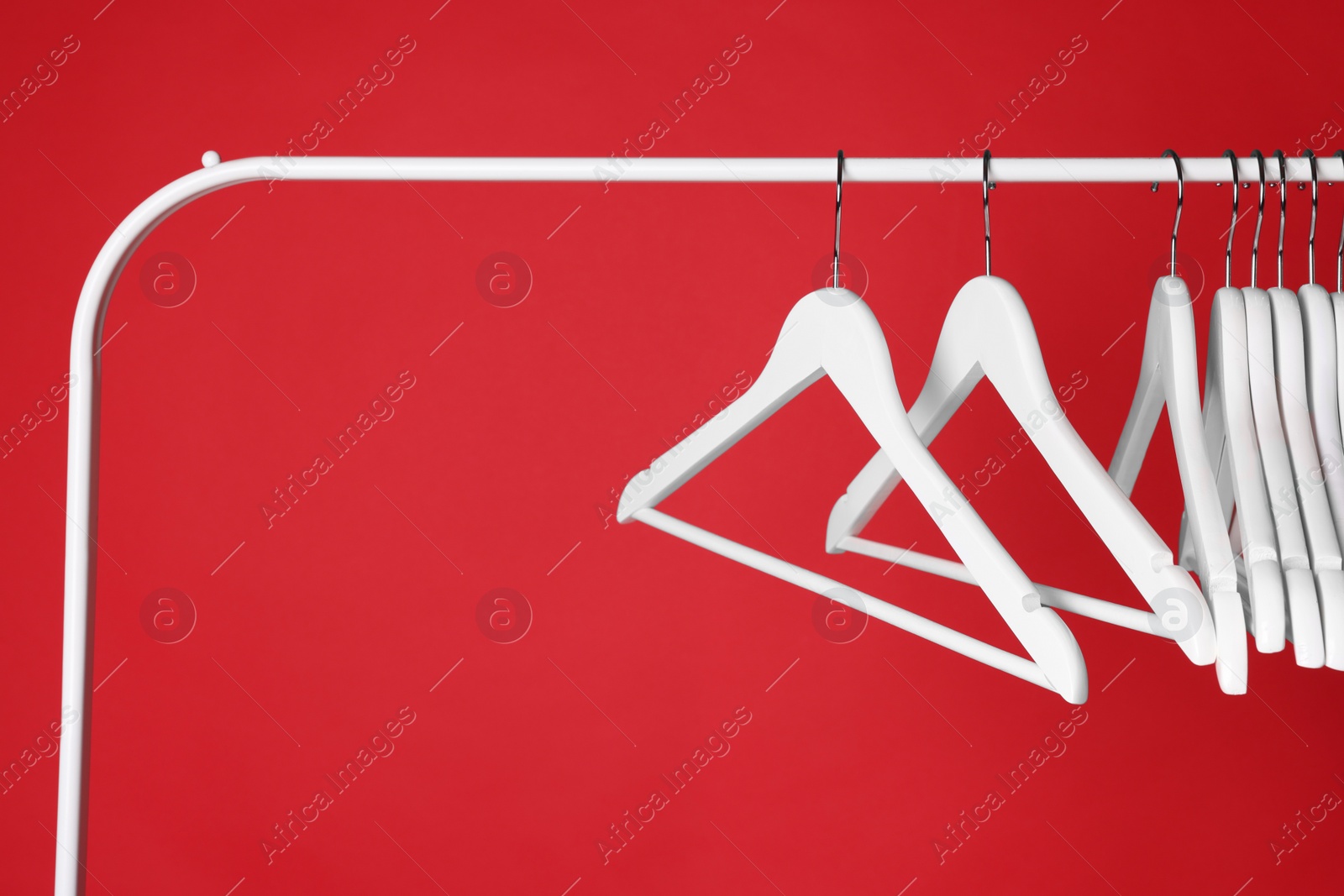 Photo of White clothes hangers on metal rack against red background