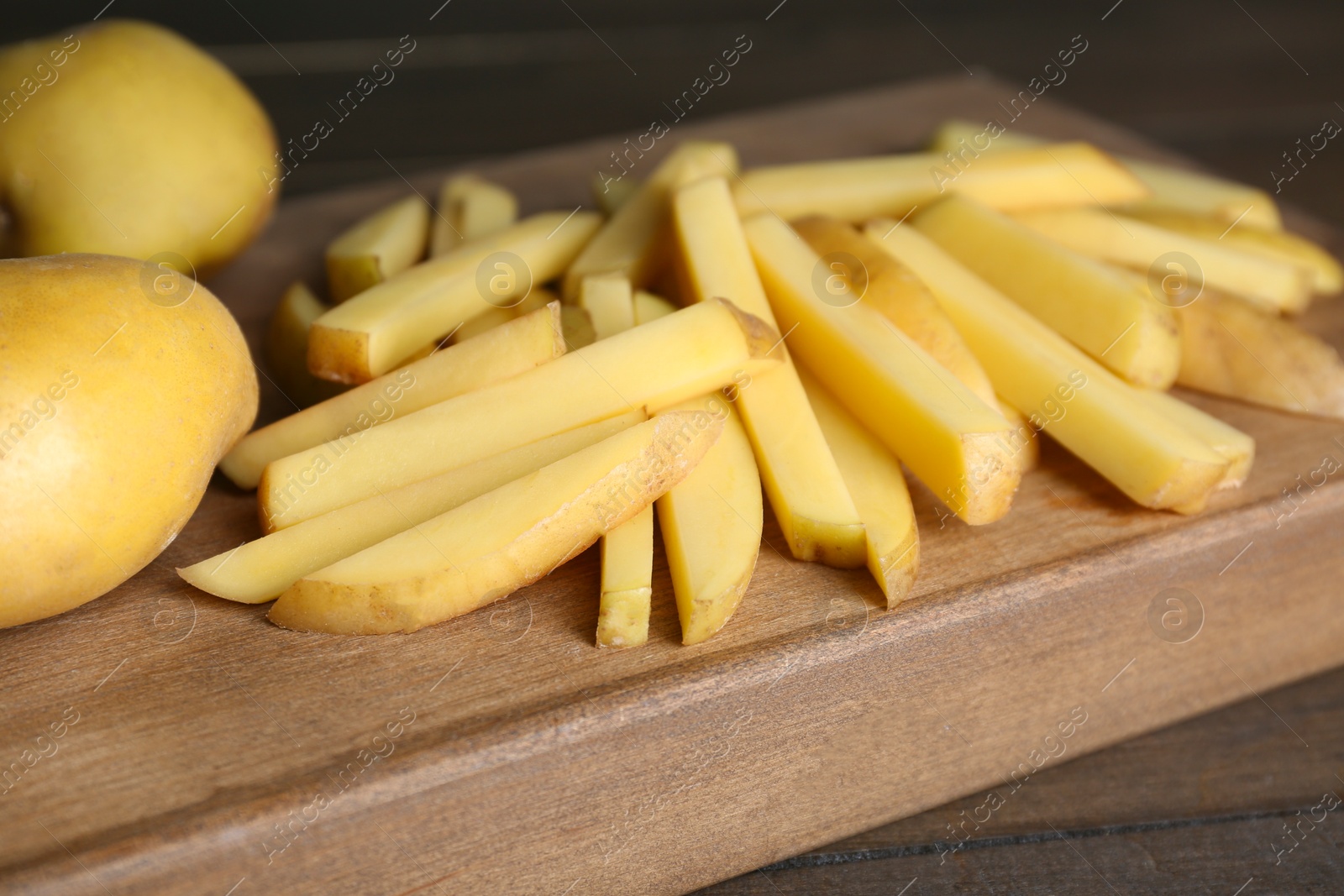 Photo of Whole and cut raw potatoes on wooden table, closeup. Cooking delicious French fries