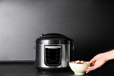 Young woman preparing food with modern multi cooker on table
