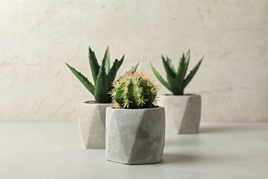 Photo of Artificial plants in cement flower pots on table against light background