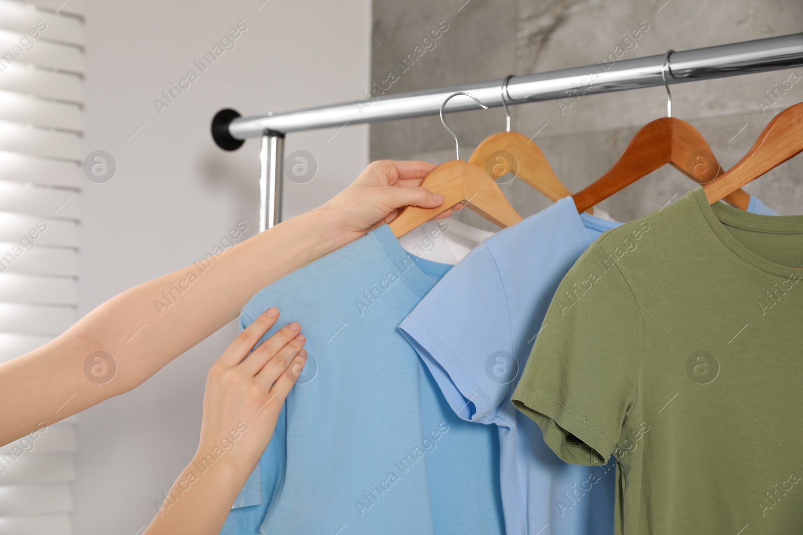 Photo of Woman hanging clean T-shirts on rack indoors, closeup