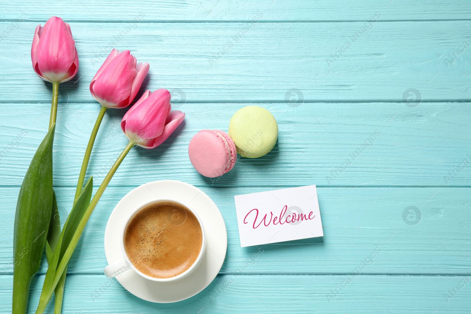 Image of Welcome card, beautiful pink tulips, macarons and cup of coffee on light blue wooden table, flat lay
