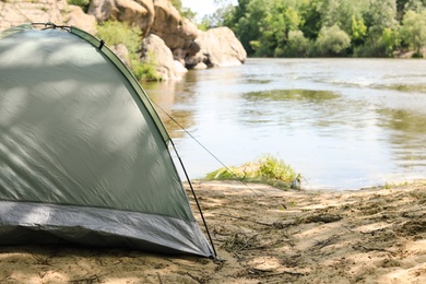 Photo of Modern camping tent on riverbank in wilderness. Space for text