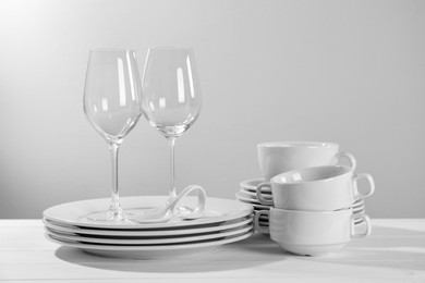 Photo of Set of clean dishware and glasses on white wooden table against light background