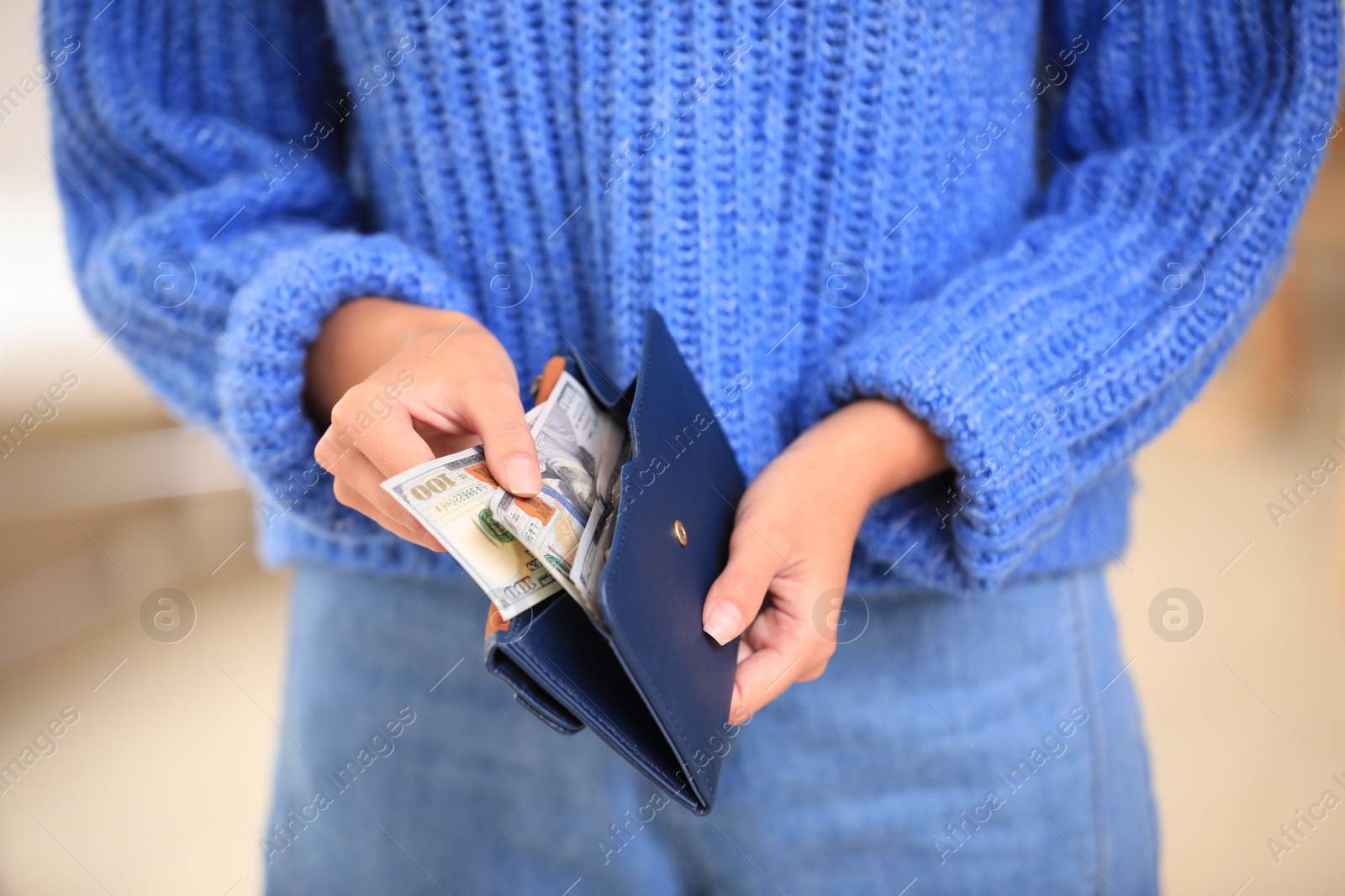 Photo of Young woman holding wallet with dollar bills on blurred background, closeup
