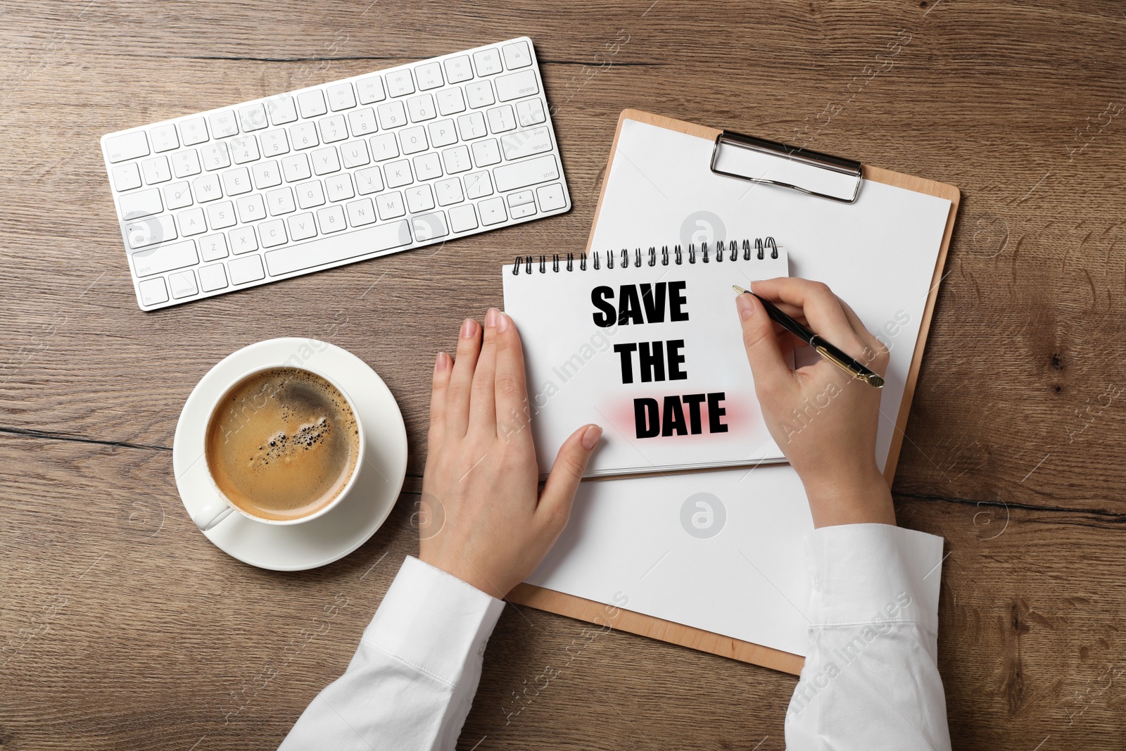 Image of Woman writing phrase SAVE THE DATE in notebook at wooden table, top view