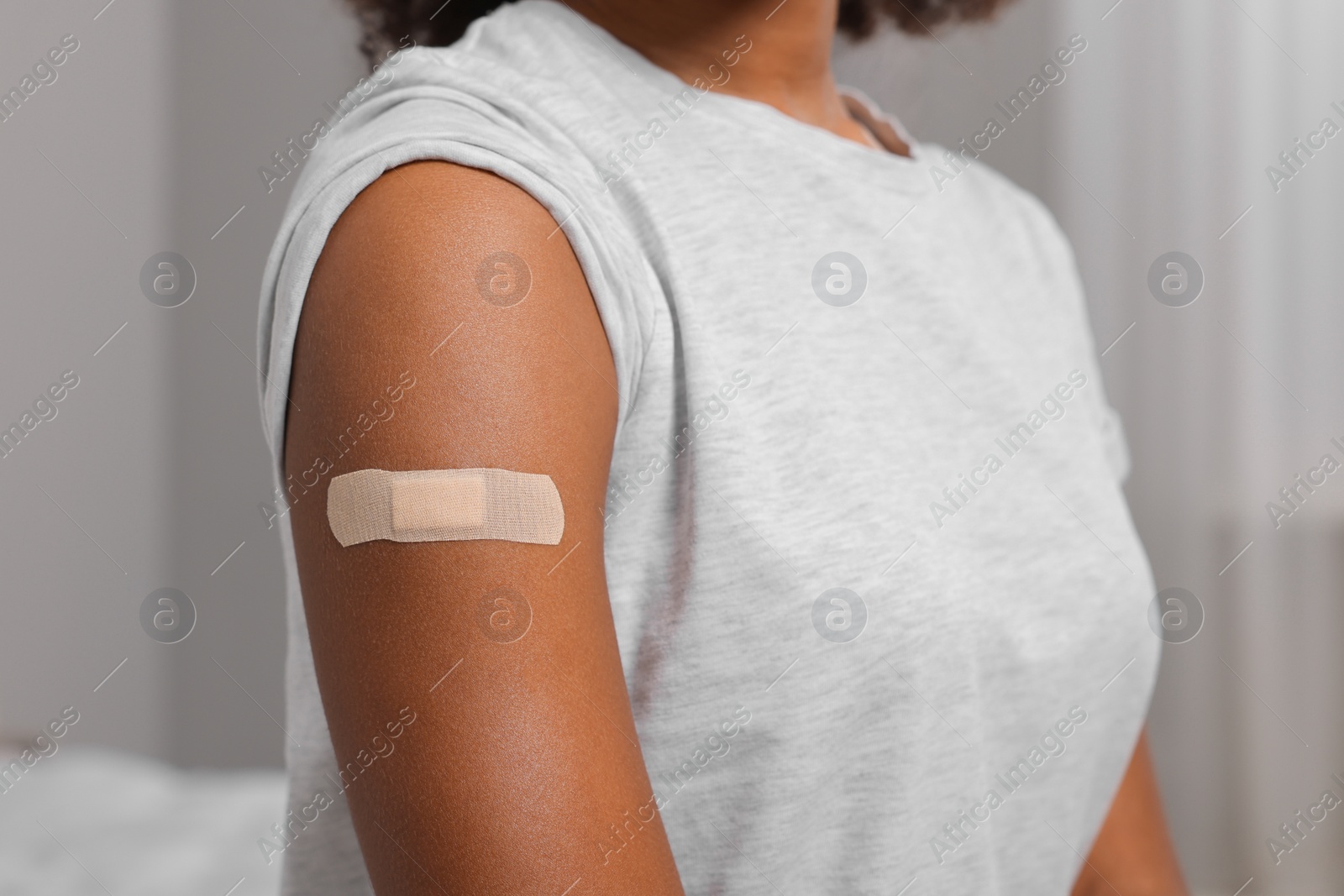 Photo of Young woman with adhesive bandage on her arm after vaccination indoors, closeup