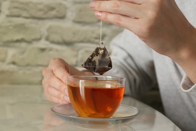 Photo of Woman taking tea bag out of cup at table indoors, closeup