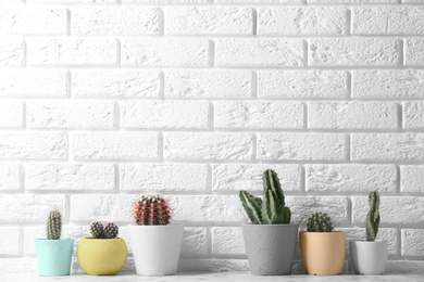 Different potted cacti on table near brick wall, space for text. Interior decor