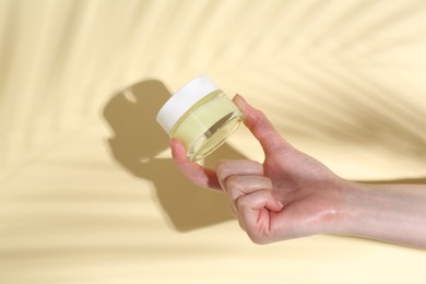 Woman holding jar of cream on yellow background, closeup