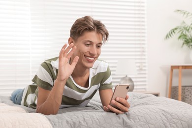 Happy young man having video chat via smartphone on bed indoors