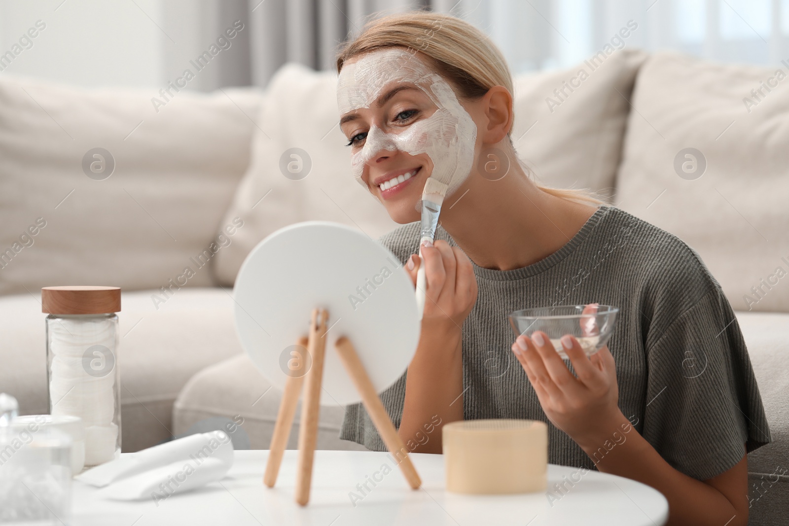 Photo of Young woman applying face mask in front of mirror at home. Spa treatments