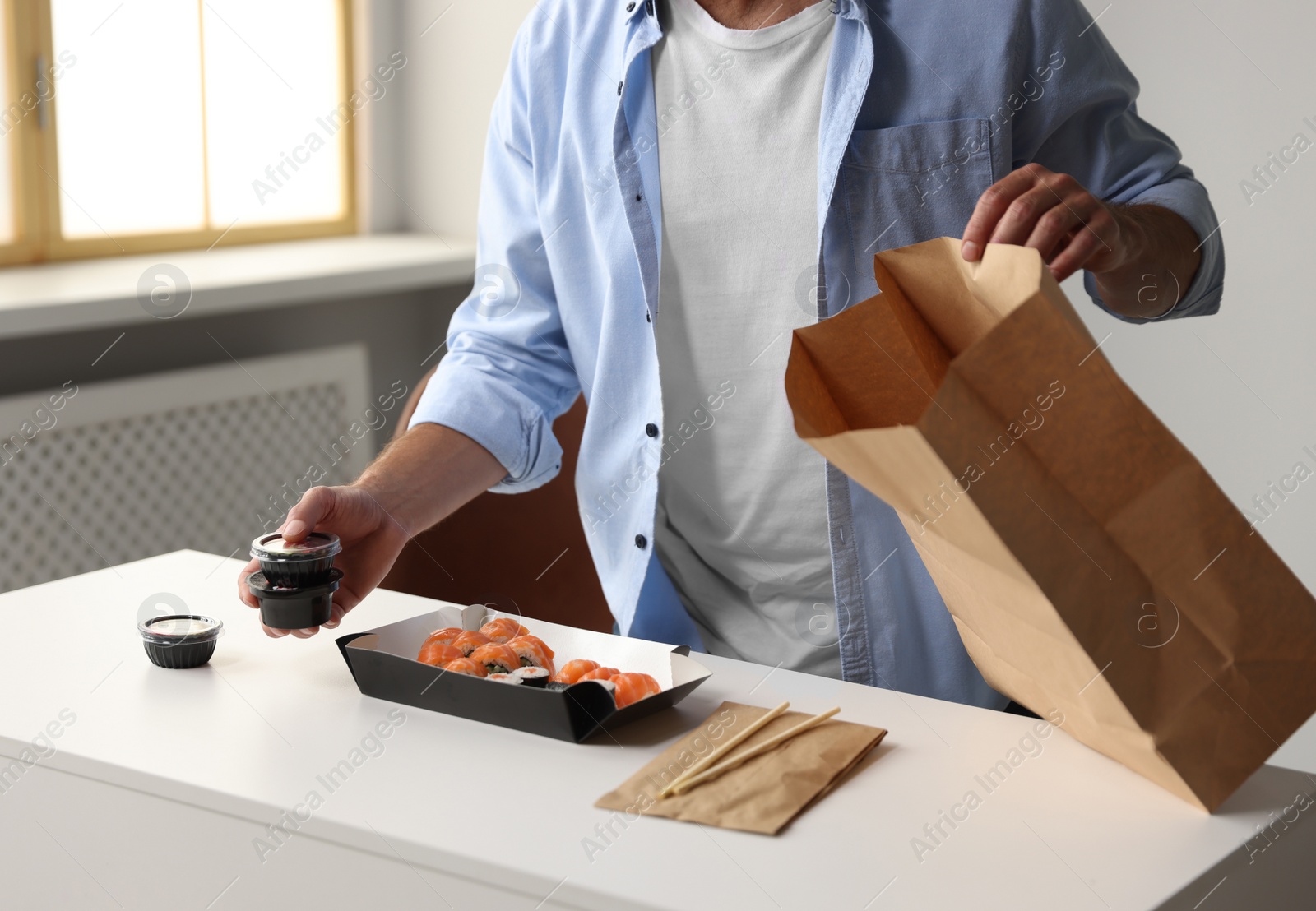 Photo of Man unpacking his order from sushi restaurant at table in room, closeup