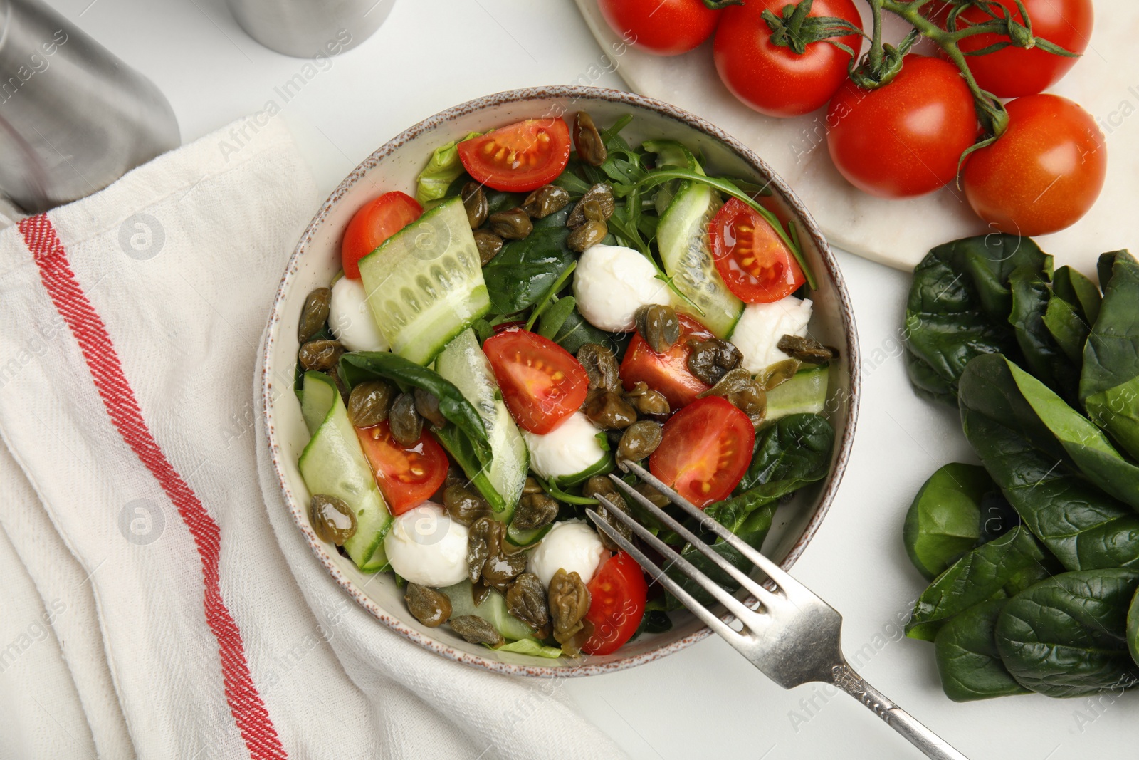 Photo of Salad with vegetables, capers and mozzarella in bowl on white table, flat lay