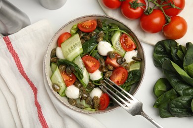 Salad with vegetables, capers and mozzarella in bowl on white table, flat lay