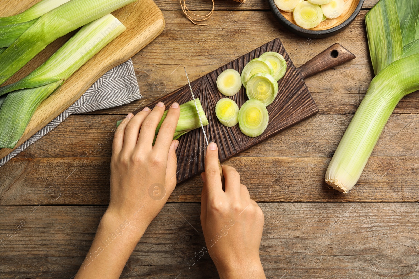 Photo of Woman cutting fresh raw leek on wooden table, flat lay. Closeup view of ripe onion