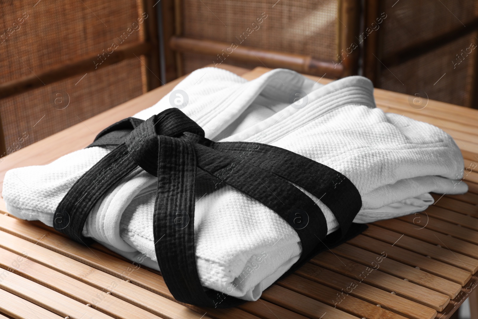 Photo of Martial arts uniform with black belt on table indoors