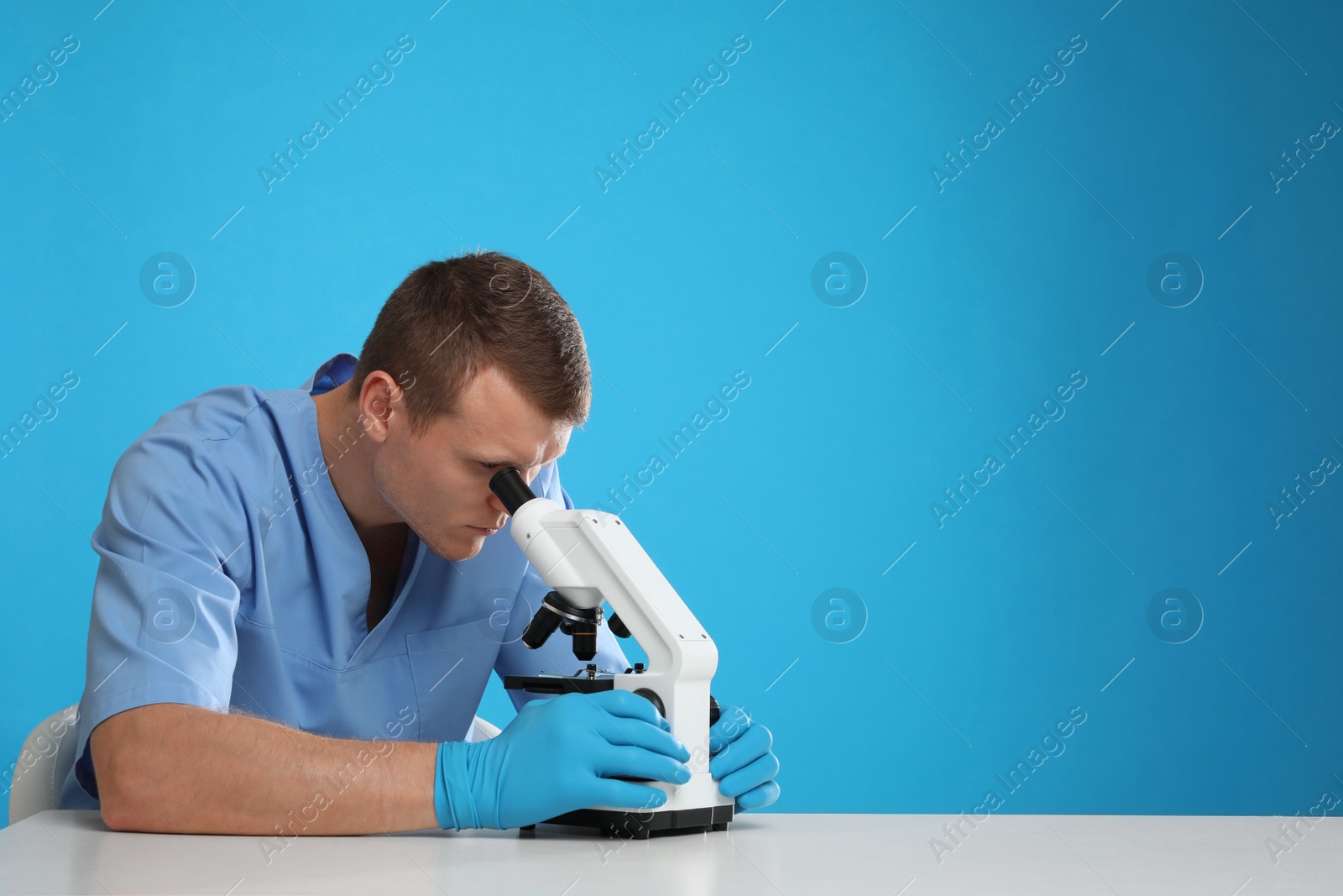 Photo of Scientist using modern microscope at table against blue background, space for text. Medical research