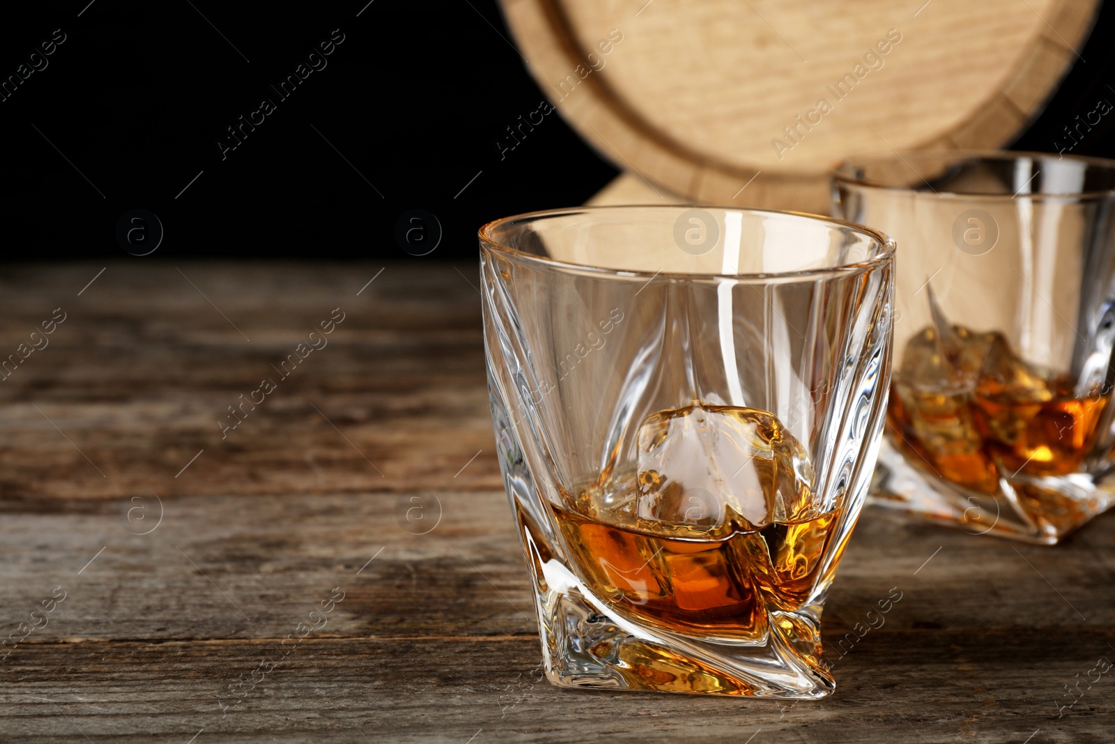 Photo of Golden whiskey in glass with ice cube on wooden table