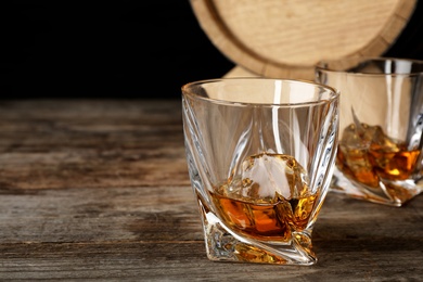 Photo of Golden whiskey in glass with ice cube on wooden table