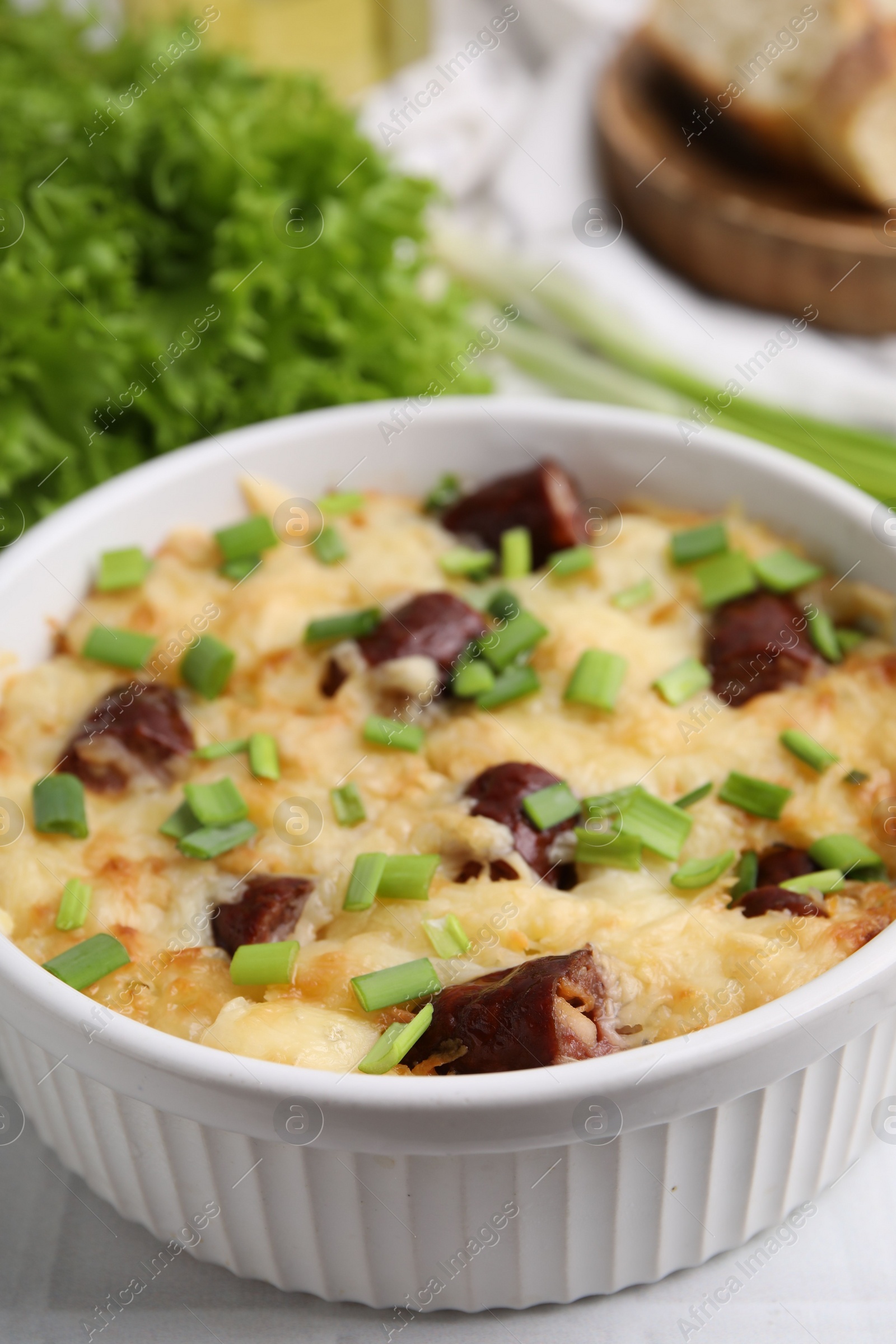 Photo of Tasty sausage casserole with green onion in baking dish on white table, closeup